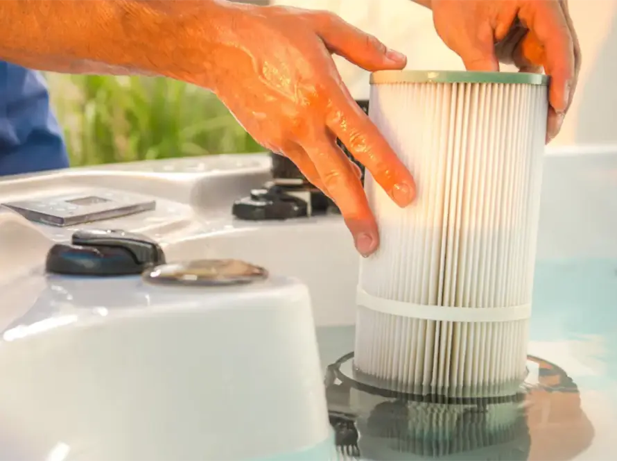 Close-up of hands performing hot tub maintenance by installing or removing a cylindrical pleated filter from the water, with control knobs and part of the hot tub visible in the foreground—ideal for spa care in the UAE.